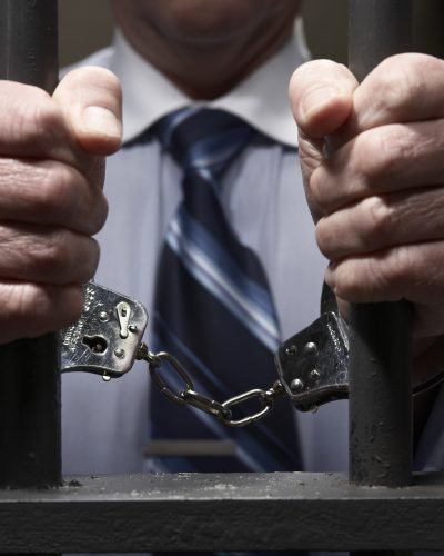 Man in handcuffs, holding prison bars, mid section, close-up of hands